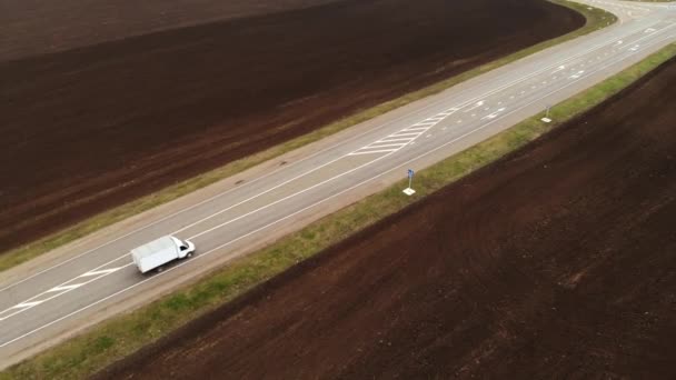 Vista aérea de una autopista rural de asfalto. Los coches se mueven por la carretera. Coches y camiones conducen a lo largo de una carretera rural. Toma de aire de la carretera. Campos fluidos alrededor de la carretera — Vídeo de stock