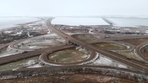 Flygfoto av bilar och lastbilar som rör sig i en vinterkorsning är en stor vägkorsning. Obemannad utsikt över biltrafiken på en motorväg i förorterna på vintern. Rondellen vid korsningen — Stockvideo