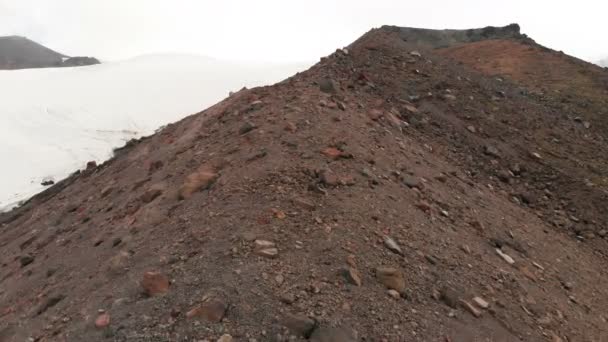 Luftaufnahme Tiefflug über Vulkangestein in den Bergen vor dem Hintergrund des Elbrus und eines großen Gletschers. Bergreise- und Kletterkonzept uhd 4k — Stockvideo