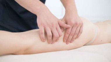 Yakın çekim bir erkek fizyoterapist pamuk bir delikanlı yanında profesyonel bir spa salonunda genç bir kadının kalça ve kalça ısınmak için hafif bir masaj yapıyor. 4k masaj vücut bakım konsepti