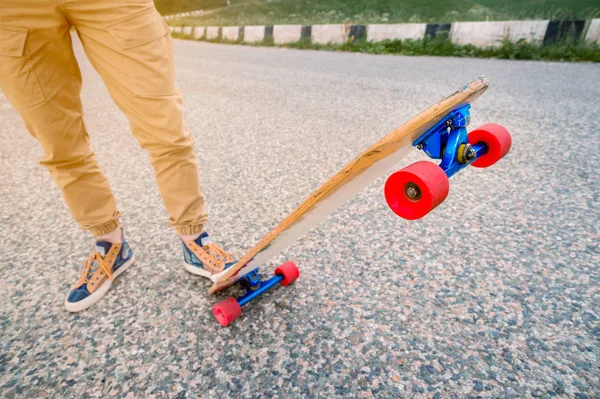Close-up de pernas masculinas em rag sneakers em um longboard no fundo de asfalto ao pôr do sol. Grande skate com pernas de homem. Conceito de lazer juvenil — Fotografia de Stock