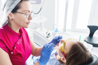 Dişçi ofisinde. Gözlüklü bir kadın diş hekimi genç bir kız hastanın çenebir döküm yapmaya hazırlanıyor. Bakım temiz ağız