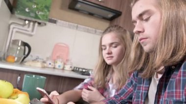 Mutfak masasında ellerinde telefonlar olan uzun saçlı bir çift tatlı kadın oturuyor. Mobil cihazlardan internet üzerinden sörf ve alışveriş. Modern genç aile kavramı