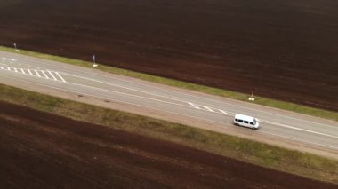 Kırsal asfalt otoyolun havadan görünüşü. Otoyol boyunca arabalar hareket ediyor. Arabalar ve kamyonlar bir kır yolu boyunca sürer. Karayolu hava görüntüleri. Yol kenarındaki tarlalar.
