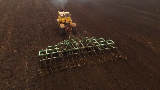Вид с воздуха на мощный желтый трактор с большим усилием на крючок, осуществляющий вспашку почвы для посева озимых культур с помощью дискового культиватора осенью — стоковое видео
