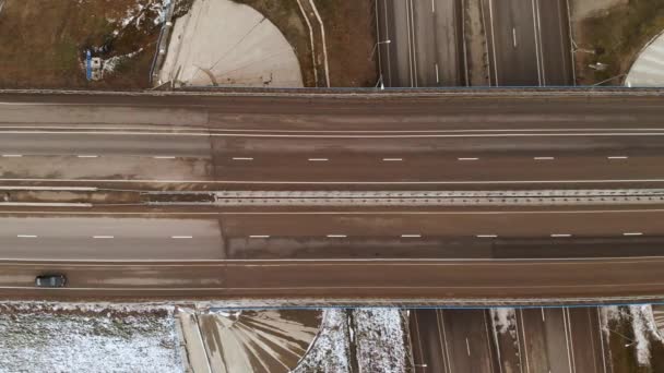 Letecký záběr shora na auta a náklaďáky pohybující se na zimní křižovatce s velkým silničním uzlem. Bezpilotní pohled na automobilovou dopravu na dálnici na předměstí v zimě. Kulatý objezd na křižovatce — Stock video