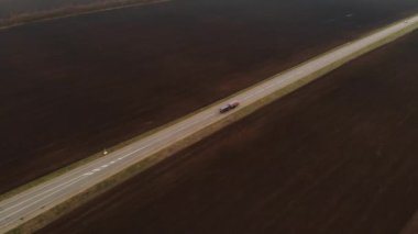 Kırsal asfalt otoyolun havadan görünüşü. Otoyol boyunca arabalar hareket ediyor. Arabalar ve kamyonlar bir kır yolu boyunca sürer. Karayolu hava görüntüleri. Yol kenarındaki tarlalar.