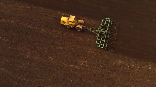 Pandangan udara dari traktor kuning yang kuat dengan upaya besar di kail yang melakukan pengolahan lahan untuk menabur tanaman musim dingin dengan kultivator cakram di musim gugur — Stok Video