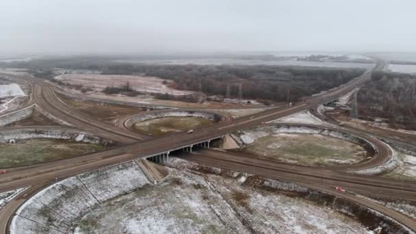 Luftaufnahmen von Autos und Lastwagen, die sich an einer winterlichen Kreuzung bewegen, sind eine große Straßenkreuzung. unbemannter Blick auf den Autoverkehr auf einer Autobahn in den Vororten im Winter. Kreisverkehr an der Kreuzung — Stockvideo