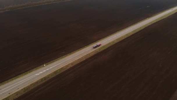 Aerial view of a rural asphalt motorway. Cars are moving along the highway. Cars and trucks drive along a country road. Highway road air footage. Plowed fields around the road — Stock Video