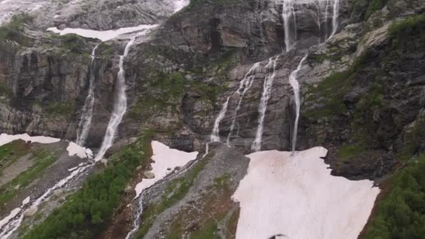 Veduta aerea drone filmato diverse cascate che scorrono lungo ripide grandi rocce alte in montagna, circondato da una vegetazione lussureggiante e non sciolta neve. Il concetto di riserve naturali del Caucaso settentrionale — Video Stock