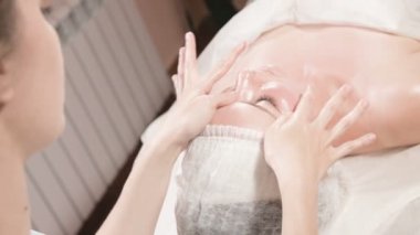 Kapalı Spa yüz masajı. Profesyonel masaj terapisti çekici bir spa salonu müşterisine yüz masajı yapıyor.