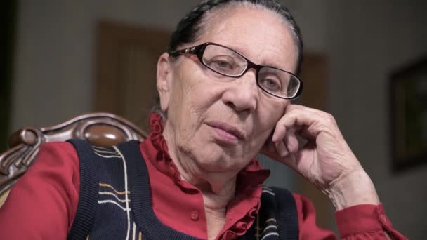 Portrait d'une femme âgée et chérissante portant des lunettes, appuyée sur son bras à l'intérieur, assise et réfléchie. Femme âgée 80 ans — Video