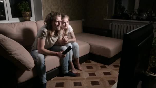 Ein junges Millennials-Paar sitzt auf der Couch vor dem Fernseher — Stockvideo