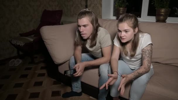 Een jong paar millennials zit op de bank voor de tv — Stockvideo