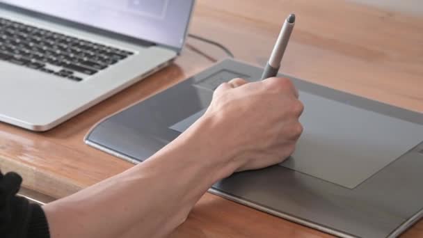 Primer plano de un diseñador masculino dibuja en su ordenador portátil con ayuda. tableta gráfica y lápiz lápiz — Vídeo de stock