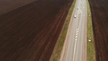 Kırsal asfalt otoyolun havadan görünüşü. Otoyol boyunca arabalar hareket ediyor. Arabalar ve kamyonlar bir kır yolu boyunca sürer. Karayolu hava görüntüleri. Yol kenarındaki tarlalar.