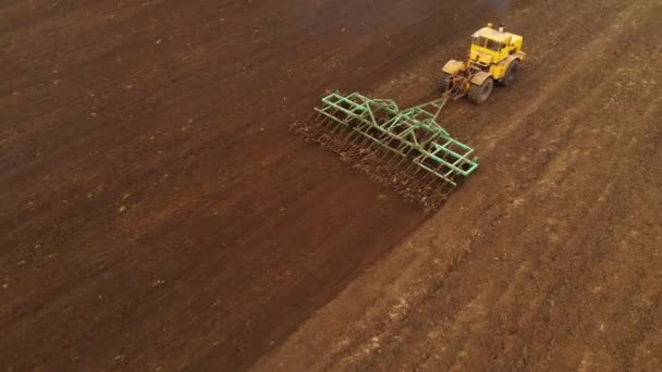 Вид с воздуха на мощный желтый трактор с большим усилием на крючок, осуществляющий вспашку почвы для посева озимых культур с помощью дискового культиватора осенью — стоковое видео