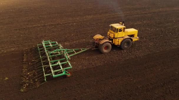 Αεροφωτογραφία ενός ισχυρού κίτρινου ελκυστήρα με μεγάλη προσπάθεια στο άγκιστρο εκτελεί άροση άροση για σπορά χειμερινές καλλιέργειες με έναν καλλιεργητή δίσκο το φθινόπωρο — Αρχείο Βίντεο