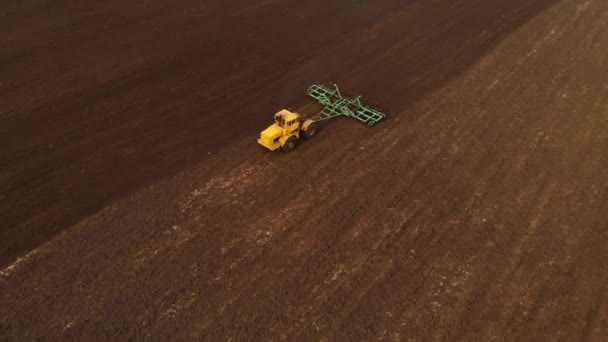 Flygfoto av en kraftfull gul traktor med stor ansträngning på kroken utför plöjning bearbetning för sådd vintergrödor med en disk kultivator på hösten — Stockvideo