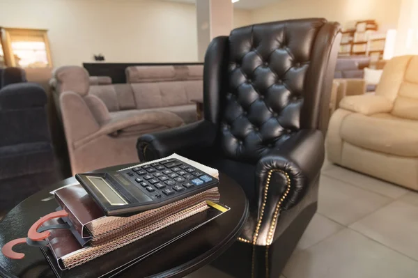 The workplace of the director of a furniture store with an expensive leather armchair, a sofa table and several catalogs of furniture and a calculator. The concept of a cozy workplace — Stock Photo, Image