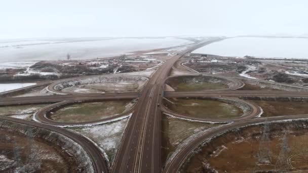 Colpo aereo di auto e camion che si muovono in un incrocio invernale è un grande incrocio stradale. Vista senza equipaggio del traffico automobilistico su un'autostrada in periferia in inverno. Rotonda all'incrocio — Video Stock