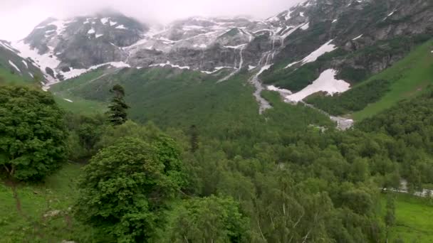 空中俯瞰低空的森林，飞向高山瀑布，那里是初夏尚未融化雪的地方。 旅游和旅行概念。 北高加索山区的瀑布 — 图库视频影像