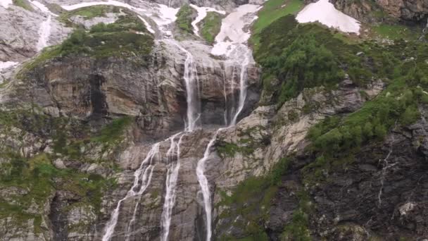 Imagens aéreas drone vista várias cachoeiras fluindo para baixo íngreme grandes rochas altas nas montanhas cercadas por vegetação exuberante e neve não derretida. O conceito de reservas naturais do Cáucaso do Norte — Vídeo de Stock