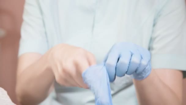 Крупним планом Професійна жінка-косметолог одягає на руки блакитні гумові чисті стерильні рукавички, перш ніж робити процедуру косметичного догляду за шкірою обличчя клієнтів . — стокове відео