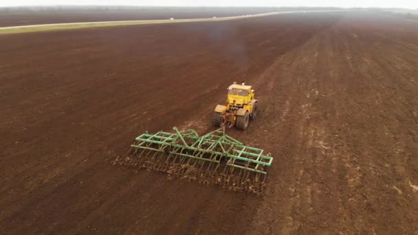 Luftaufnahme eines gelben Traktors mit Anhänger, der ein Land pflügt, bevor er Getreide anpflanzt. das Konzept der Bodenvorbereitung für die Aussaat von Saatgut im Boden. Bauernhof — Stockvideo