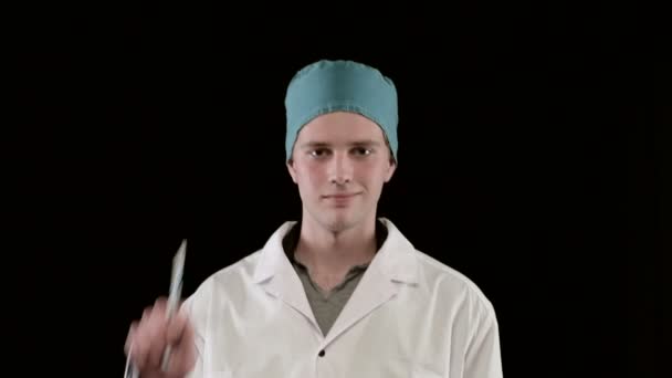 Νεαρός με ιατρικό παλτό, δείχνει δύο σύριγγες στο χέρι. Μαύρο φόντο, κοντινό πλάνο. — Αρχείο Βίντεο