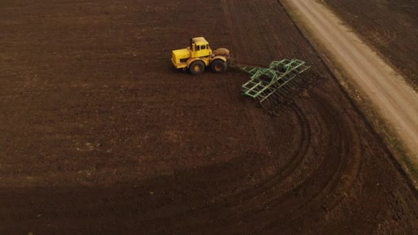 Veduta aerea di un trattore giallo con un rimorchio arare un terreno arare un campo coltivato prima di piantare cereali. Il concetto di preparare il terreno per piantare semi nel terreno. Azienda agricola — Video Stock