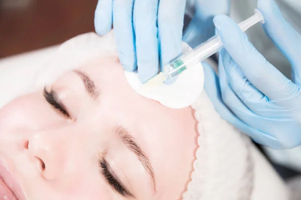 Close-up Jovem atraente recebe injeções faciais anti-envelhecimento. Ela se deita calmamente em uma clínica ou salão. Um jovem cosmetologista experiente enche rugas femininas com ácido hialurônico de uma seringa — Fotografia de Stock