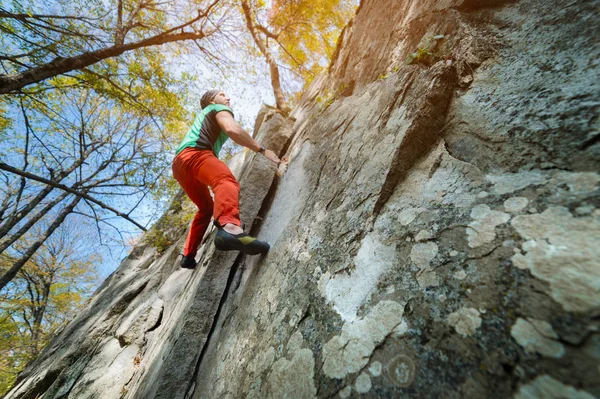 Ein frei gealterter männlicher Kletterer hängt an einer Felswand in einem Wald in den Bergen. Reifes Sportkonzept — Stockfoto