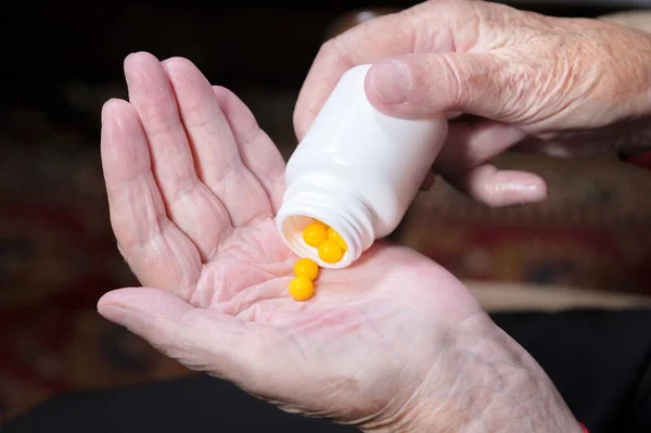 Manos de una anciana sosteniendo un frasco blanco con cápsulas medicinales omega-3 y vitaminas. Concepto de salud suplementos píldoras y vitaminas —  Fotos de Stock