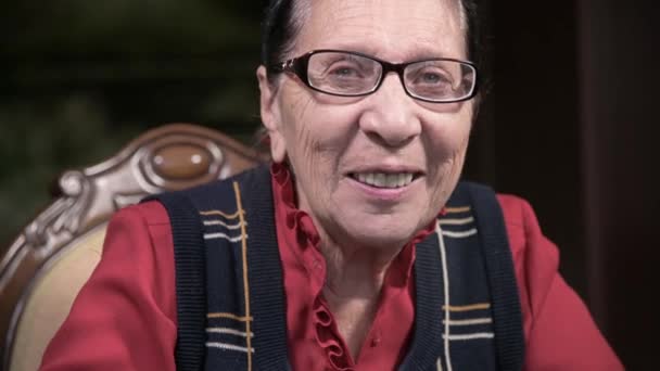 Retrato de una anciana sonriente con gafas apoyadas en su brazo, sentada y pensando. Mujer mayor 80 años — Vídeo de stock