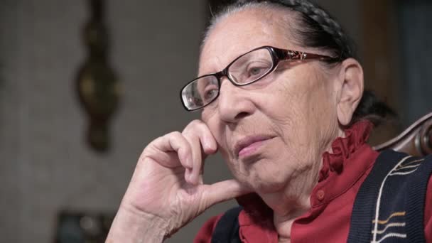 Portrait d'une femme âgée et chérissante portant des lunettes, appuyée sur son bras à l'intérieur, assise et réfléchie. Femme âgée 80 ans — Video