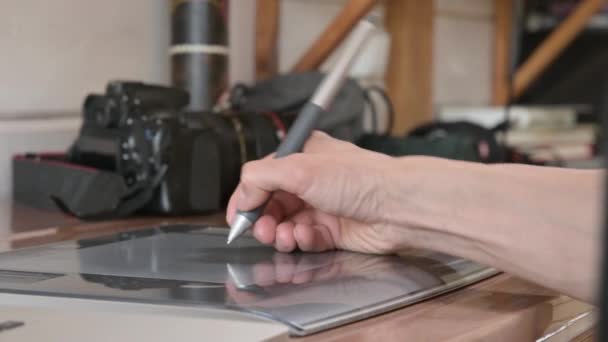 Close-up van een mannelijke ontwerper trekt met hulp op zijn laptop. grafische tablet en pen stylus Tegen de achtergrond van zijn Slr camera — Stockvideo