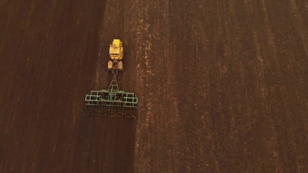 Vista aérea de un tractor amarillo con un remolque arando una tierra arando un campo cultivado antes de plantar cereales. El concepto de preparar la tierra para la siembra de semillas en el suelo. Granja — Vídeos de Stock