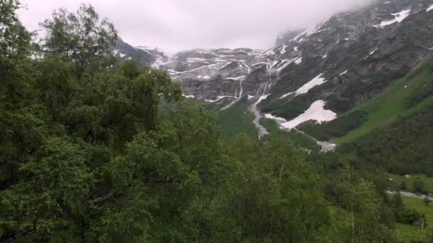 Letecký pohled nízko nad lesem na vysokohorské vodopády s místy neroztaveného sněhu na začátku léta. Cestovní ruch a pojetí cestování. Vodopády v horách severního Kavkazu — Stock video