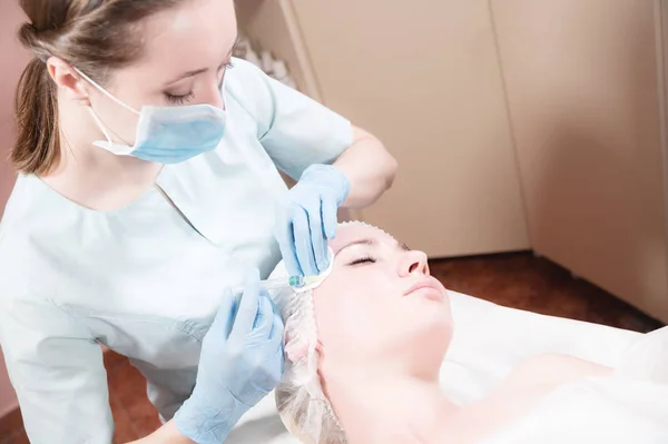 Close-up Jovem atraente recebe injeções faciais anti-envelhecimento. Ela se deita calmamente em uma clínica ou salão. Um jovem cosmetologista experiente enche rugas femininas com ácido hialurônico de uma seringa — Fotografia de Stock