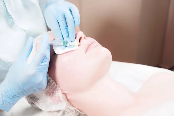 Close-up Mujer joven atractiva recibe inyecciones faciales antienvejecimiento. Se acuesta tranquilamente en una clínica o salón. Un joven cosmetólogo experimentado llena las arrugas femeninas con ácido hialurónico de una jeringa — Foto de Stock