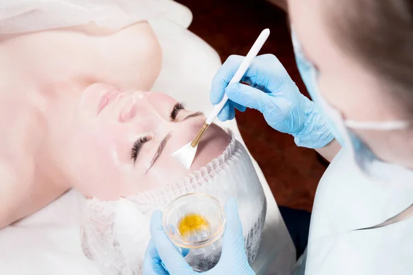 Chica esteticista aplica un cepillo para rejuvenecer una máscara en la cara de una chica atractiva en un salón de spa. El concepto de autocuidado y rejuvenecimiento — Foto de Stock