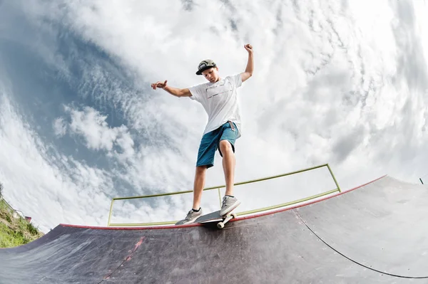 Portret van een jonge skateboarder die een truc uithaalt op zijn skateboard op een halfpipe helling in een skatepark in de zomer op een zonnige dag. Het begrip jongerencultuur van vrijetijdsbesteding en sport — Stockfoto