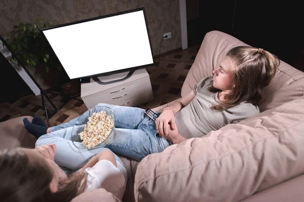 Una giovane coppia di semi che guarda un film sdraiata su un divano la sera nel loro appartamento con una ciotola di popcorn. Lo schermo della TV si è spento. Designer vuoto grandangolo — Foto Stock