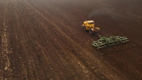 Вид с воздуха на желтый трактор с прицепом, вспахивающим землю перед посадкой зерновых. Концепция подготовки почвы для посадки семян в почву. Ферма — стоковое видео