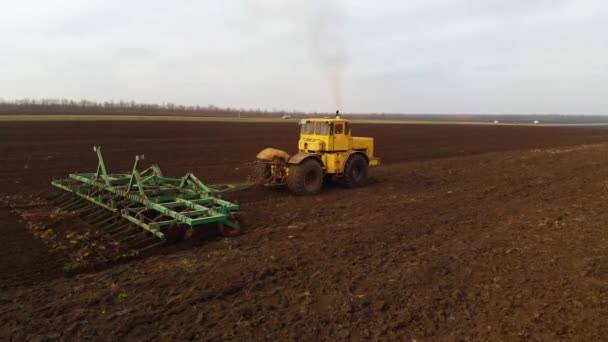 Luftaufnahme eines gelben Traktors mit Anhänger, der ein Land pflügt, bevor er Getreide anpflanzt. das Konzept der Bodenvorbereitung für die Aussaat von Saatgut im Boden. Bauernhof — Stockvideo