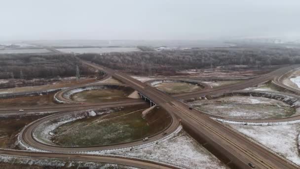 Zdjęcie lotnicze samochodów osobowych i ciężarowych poruszających się na zimowym skrzyżowaniu to duży węzeł drogowy. Bezzałogowy widok ruchu samochodowego na autostradzie na przedmieściach w zimie. Karuzela na skrzyżowaniu — Wideo stockowe