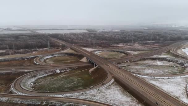 Flygfoto av bilar och lastbilar som rör sig i en vinterkorsning är en stor vägkorsning. Obemannad utsikt över biltrafiken på en motorväg i förorterna på vintern. Rondellen vid korsningen — Stockvideo