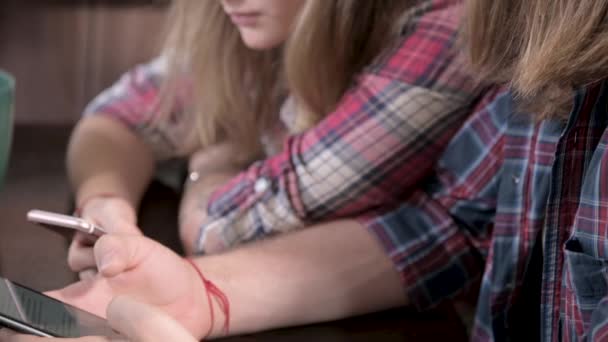 Close-up Um jovem par de mellenials com cabelos longos estão sentados na mesa da cozinha com telefones em suas mãos. Navegar e fazer compras na Internet a partir de dispositivos móveis. Conceito de família jovem moderna — Vídeo de Stock